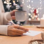 Hand schreibt mit einem Stift weihnachtliche Worte auf Papier